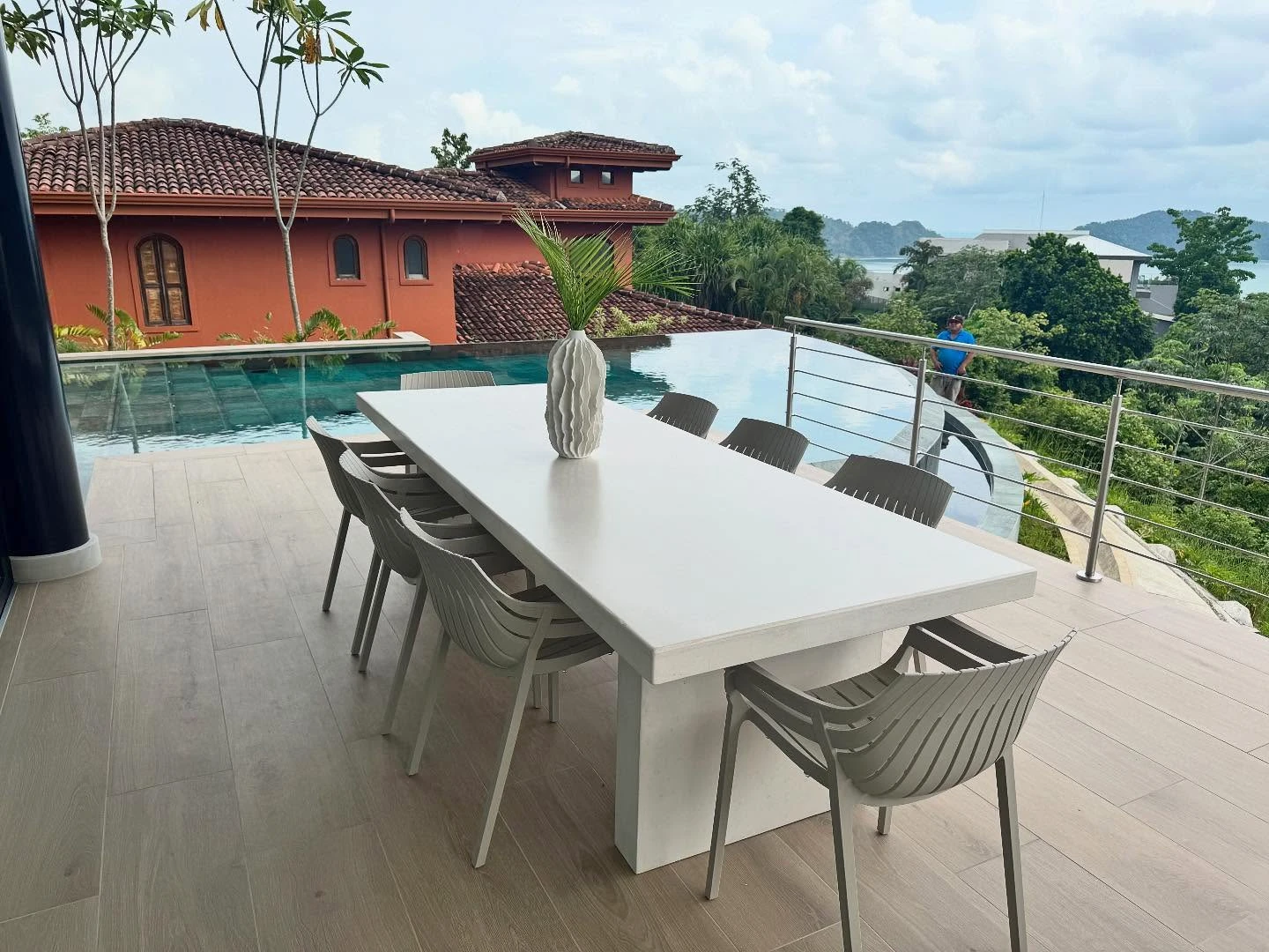 Mesa rectangular de concreto blanco en una terraza junto a la piscina, con vista al mar