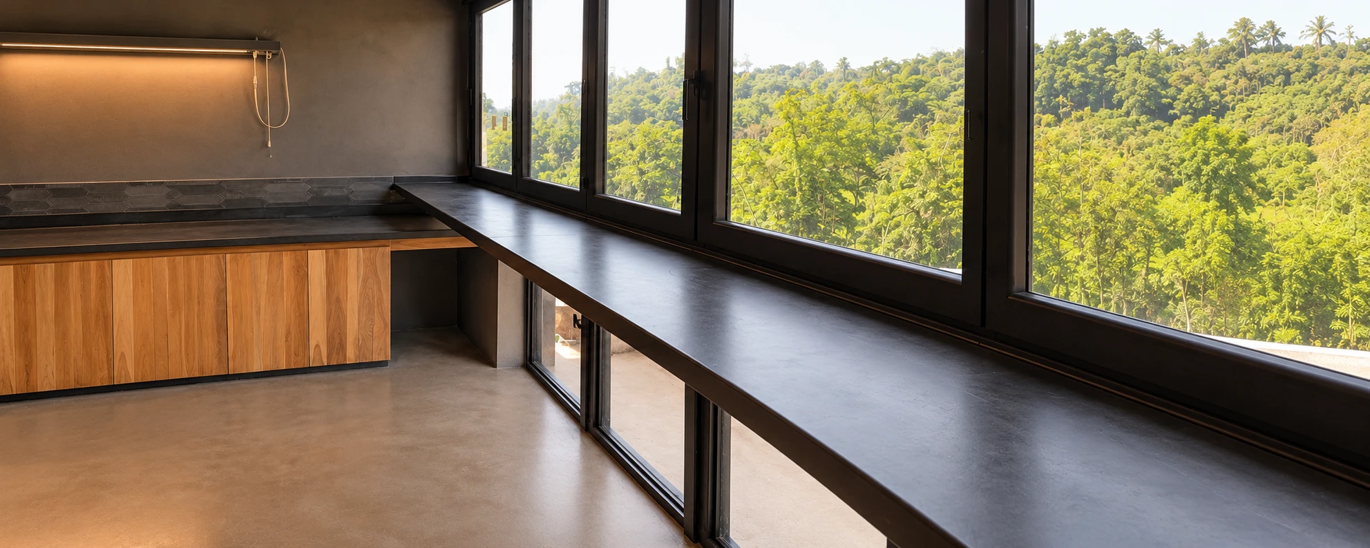Sobre corrido de concreto negro a lo largo de un ventanal con vista al bosque, junto a un mueble de madera
